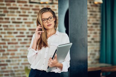 Duvara karşı dururken akıllı telefon kullanarak iş kadını. Dizüstü tutan diğer elinde.