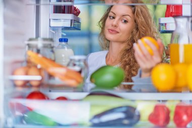 Açılan buzdolabı önünde duran ve turuncu meyve kadın. Dolap dolusu yiyecek.