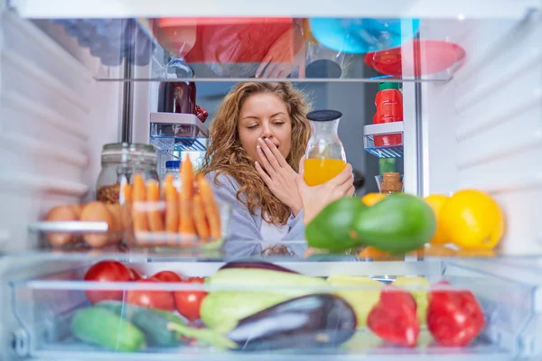 Woman taking juice from fridge full of groceries. Picture taken from the inside of fridge. Morning routine.