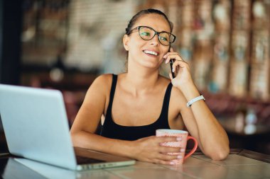 Akıllı telefon ve holding kupa restoranda otururken kullanan kadın.