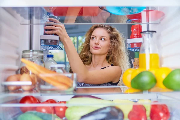 Woman taking jar from fridge full of groceries ato make a breakfast. Picture taken from the inside of fridge.