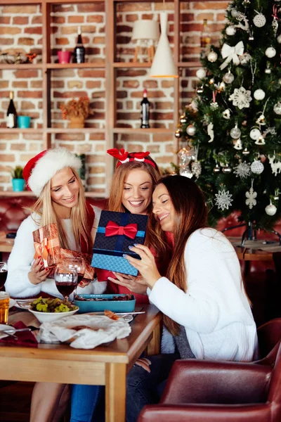 Friends giving gifts to each other while sitting at table. In background Christmas tree. Christmas holidays concept.