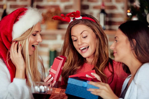 Friends giving gifts to each other while sitting at table. In background Christmas tree. Christmas holidays concept.