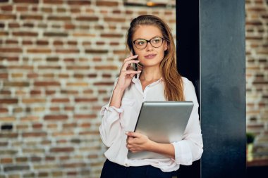 Duvara karşı dururken akıllı telefon kullanarak iş kadını. Dizüstü tutan diğer elinde.