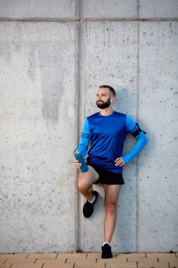 Dinlenme ve elinde şişe su ile tutarak duvara karşı duran erkek atlet. Sağlıklı yaşam konsepti.