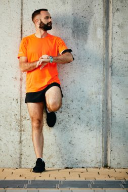 Genç adam duvara karşı ayakta ve kronometre bileğinde ayarlama sakallı. Sağlıklı yaşam konsepti.