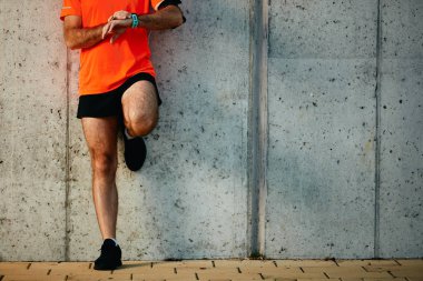 Genç adam duvara karşı ayakta ve kronometre bileğinde ayarlama sakallı. Sağlıklı yaşam konsepti.