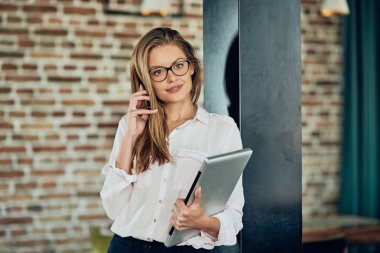 Duvara karşı dururken akıllı telefon kullanarak iş kadını. Dizüstü tutan diğer elinde.