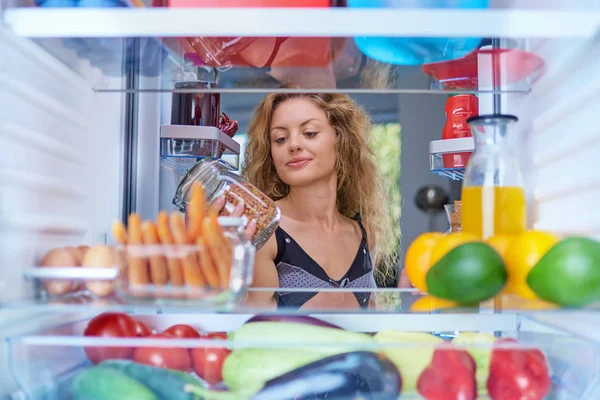 Woman taking food from fridge full of groceries. Picture taken from the inside of fridge.