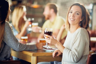 Kameraya bakarak ve şarap restoranda otururken tutan kadın. İçki ve sohbet arka plan arkadaşlar.