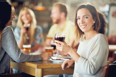 Kameraya bakarak ve şarap restoranda otururken tutan kadın. İçki ve sohbet arka plan arkadaşlar.