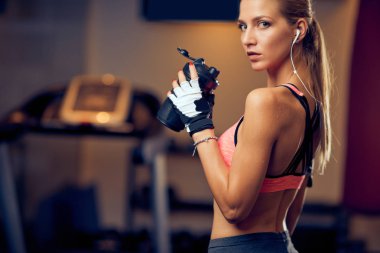 Woman drinking water and looking over the shoulder. Gym interior. clipart