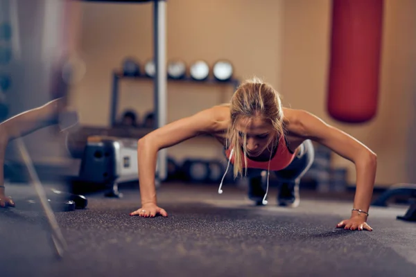 Sporty woman doing push-ups on the floor. In background exercise equipment. Gym interior.