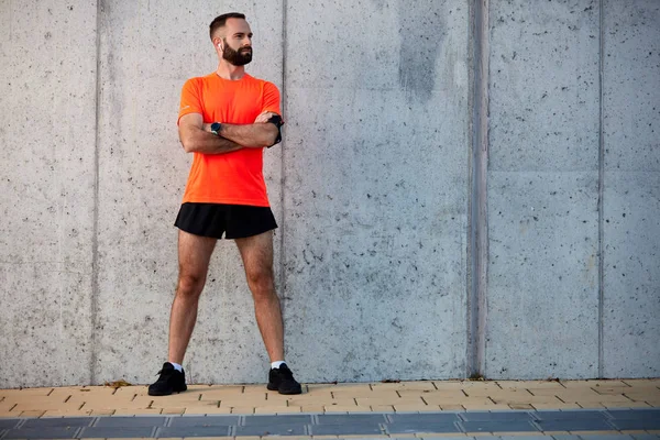 Male runner standing with crossed arms in sportswear outdoors. Healthy lifestyle concept.