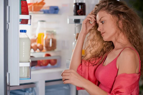 Woman standing in front of fridge full of groceries and looking something to eat. Picture taken from the inside of fridge.