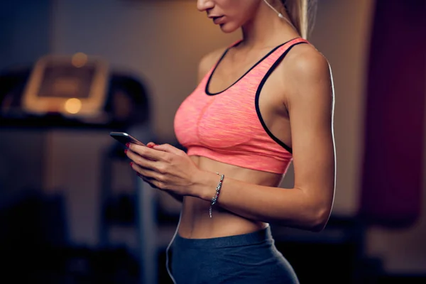 关闭的妇女使用智能手机短信 阅读信息 而站在健身房 健康的生活方式概念 — 图库照片
