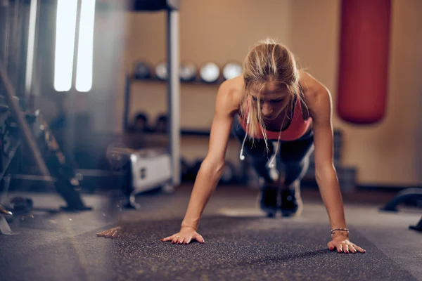 运动的女人在地板上做俯卧撑 在后台锻炼设备 健身房内饰 — 图库照片