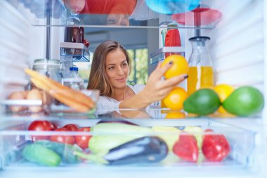 Açılan buzdolabı önünde duran ve turuncu meyve kadın. Buzdolabı yiyecek dolu. Resim buzdolabı Iside alınan.