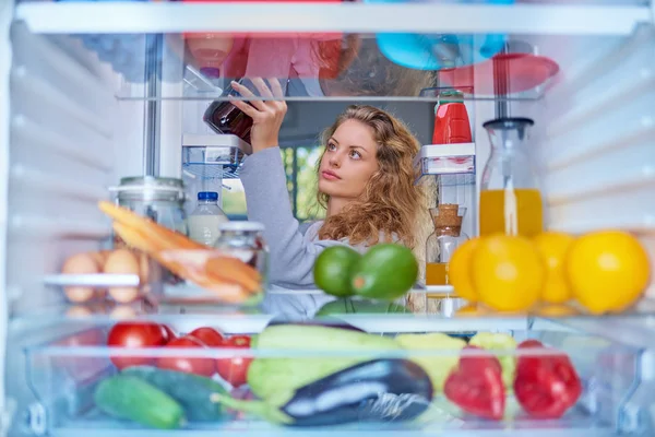 Woman taking food from fridge full of groceries. Picture taken from the inside of fridge.