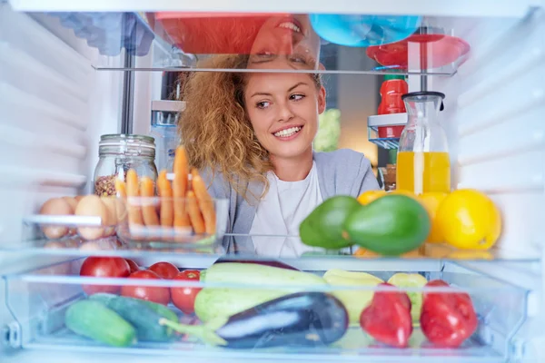 Woman standing in front of fridge full of groceries and looking something to eat. Picture taken from the inside of fridge.