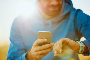 Genç sakallı adam akıllı bakarak ve akıllı telefon diğer elinde tutan kullanarak yakın çekim.