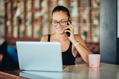 Restoranda otururken akıllı telefon ve dizüstü bilgisayar kullanan beyaz kadın. Danışma laptop ve kupa çay ile.