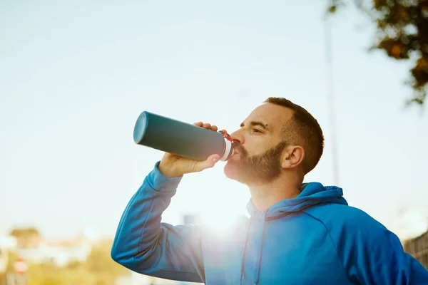 Close up of young bearded sporty man drinking water. Healthy lifestyle concept.