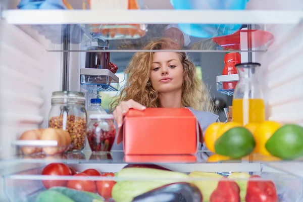 Woman taking box with donuts from fridge full of groceries. Picture taken from the inside of fridge.