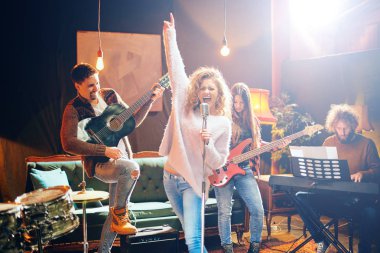 Caz Orkestrası Konser için hazırlanıyor. Ön plan kadının grubun geri kalanı şarkı bas gitar, clavier ve akustik gitar oynamak. Ev müzik stüdyosu iç.