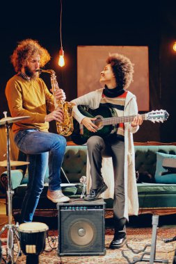 Karışık ırk kadın adam saksafon oynamaya akustik gitar çalmak. Ev stüdyosu iç.