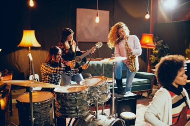 Caz müzik kızlar. Ön planda bir kadın bas gitar çalıyor ve arka plan diğer üç akustik gitar, saksafon ve davul çalmaya. Ev stüdyosu iç.