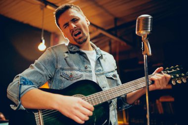 Sakallı Kafkas müzisyen akustik gitar çalıyor ve şarkı. Ev stüdyosu iç.