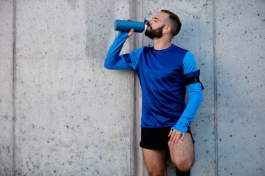 Adam çalıştıran ve içme suyu duvara karşı dururken dinleniyor. Sağlıklı yaşam konsepti.