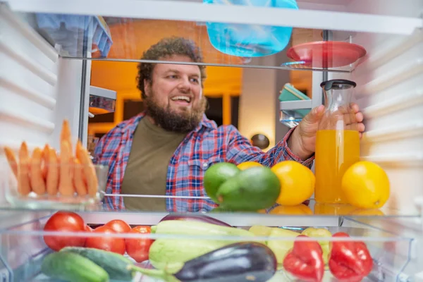 Man looking for something to eat at night while standing in front of opened fridge. Unhealthy eating concept. Picture taken from the inside of fridge.