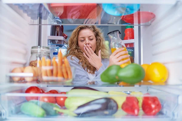 Woman standing in front of fridge full of groceries and taking juice. Picture taken from inside of fridge.