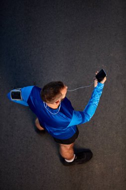 Üstten görünüm sokakta duran ve smartphone kullanarak koşucu. Sağlıklı yaşam konsepti.