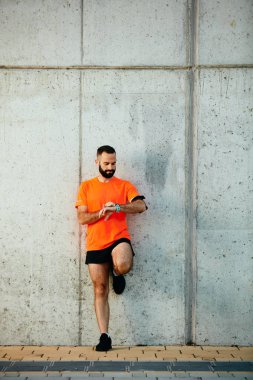Genç adam duvara karşı ayakta ve kronometre bileğinde ayarlama sakallı. Sağlıklı yaşam konsepti.