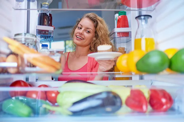 Woman taking gateau form fridge full of groceries. Unhealthy eating concept. Picture taken from the inside of fridge.