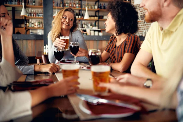 Restoranda oturan ve şarap ve bira içme çok kültürlü arkadaşlar.