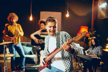 Şarkı ve ev stüdyosunda otururken bas gitar çalmaya dostum. İçinde kendi grubu aletleri oynamak arka plan.
