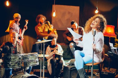 Caz Orkestrası Konser için hazırlanıyor. Ön plan kadının grubun geri kalanı şarkı bas gitar, clavier ve akustik gitar oynamak. Ev müzik stüdyosu iç.