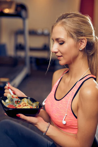 Side view of woman eating healthy food while sitting in a gym. Healthy lifestyle concept.