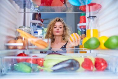 Turuncu buzdolabı kahvaltı için çekici bir kadın. Resim buzdolabının içinden çekilen.