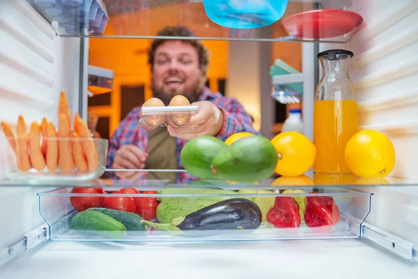 Un homme prenant des œufs du frigo pour préparer un repas tard dans la nuit. Concept de troubles de l'alimentation et de l'alimentation malsains. Photo prise de l'intérieur du réfrigérateur . — Photo