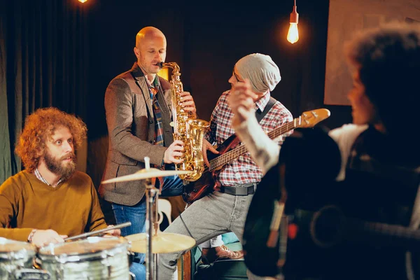 Banda multicultural praticando para o show em estúdio em casa. Em primeiro plano cantor de raça mista e no fundo baterista e saxofonista . — Fotografia de Stock