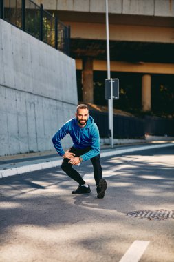 Genç erkek koşucu çalıştırmadan önce bacaklarını germe sakallı. Spor giyim, sağlıklı yaşam konsepti giyiyor.