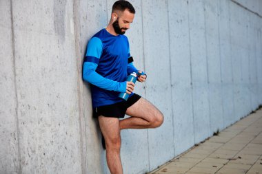 Dinlenme ve elinde şişe su ile tutarak duvara karşı duran erkek atlet. Sağlıklı yaşam konsepti.