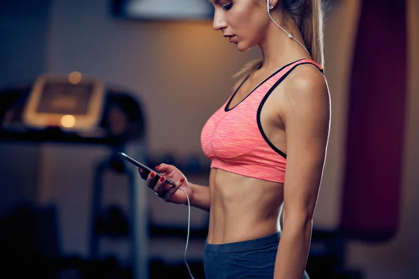 Mujer usando el teléfono inteligente mientras está de pie en el gimnasio. En cinta de correr de fondo. concepto de estilo de vida saludable . — Foto de Stock