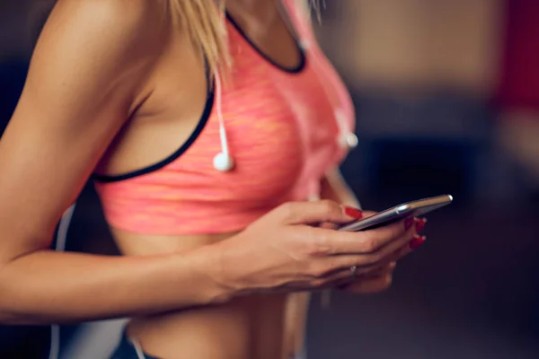 Primer plano de la mujer que usa el teléfono inteligente para enviar mensajes de texto / lectura mientras está de pie en el gimnasio. concepto de estilo de vida saludable . — Foto de Stock