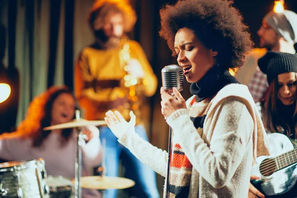 Gemengd ras vrouw zingen. In achtergrond band spelen van instrumenten. Home studio interieur. — Stockfoto